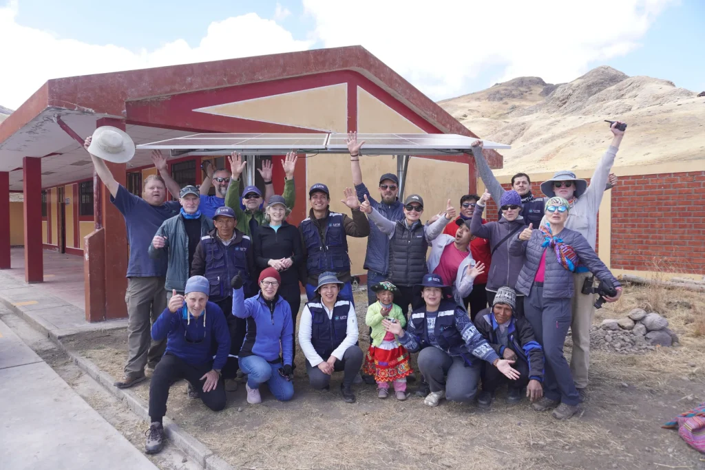 Volunteers, local families, and children celebrating in front of a school building in Patahuasi, Peru