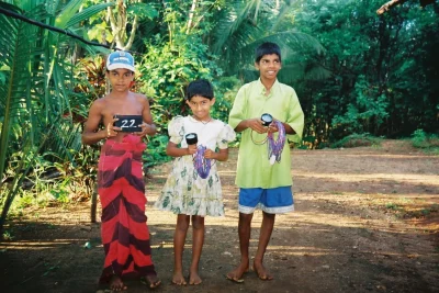 Three children in Sri Lanka holding LED lights distributed by LUTW solar energy charity in 2004