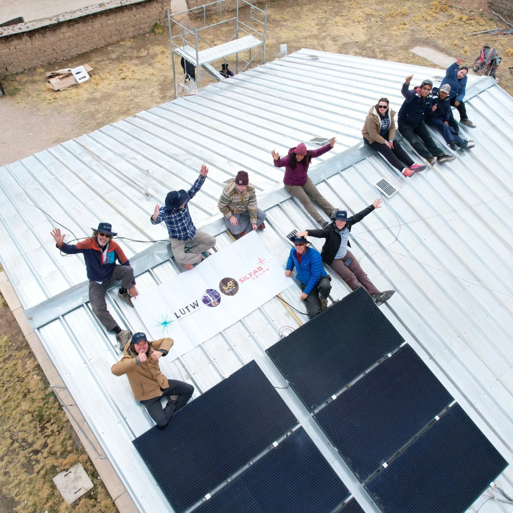 Volunteers celebrate next to newly installed solar panels at the Huarcaya health clinic, holding a banner with the LUTW logo.