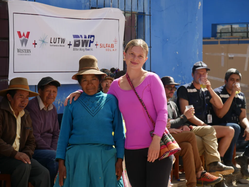 LUTW solar volunteer from Western Colorado University standing with a local community member in front of project partner logos after solar charity project
